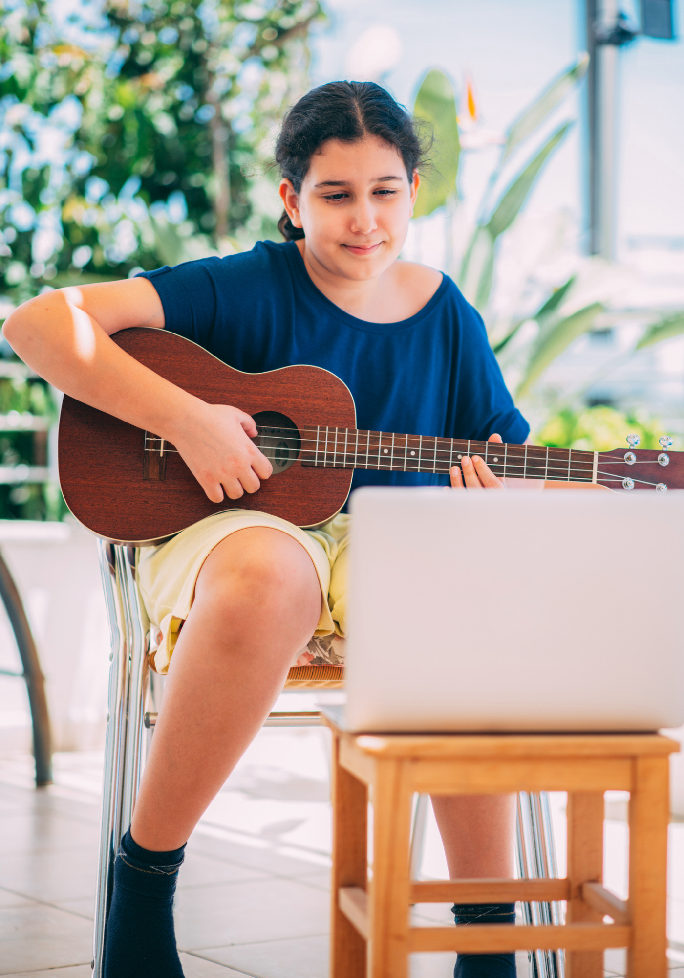 Adolescent learns how to play guitar in front of a laptop