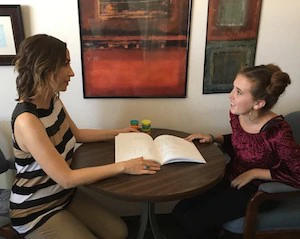 PPS-R™ program participant speaks with a facilitator who is showing her a book at a table.
